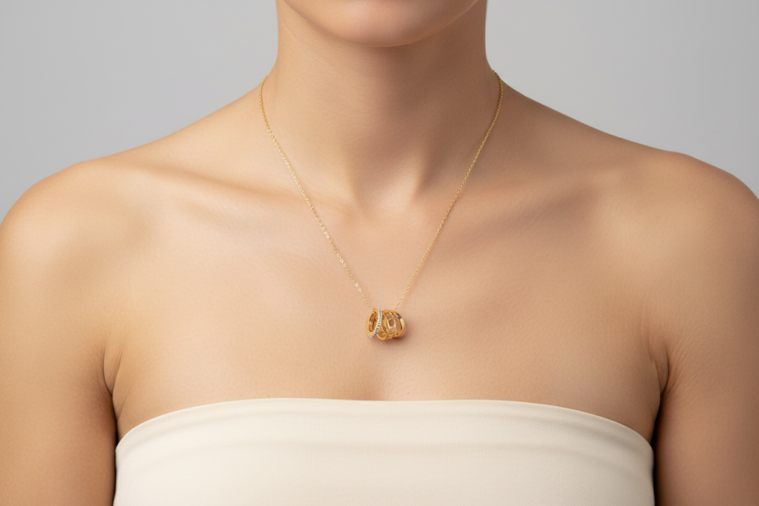 Gold necklace with a pendant on a person wearing a strapless top against a neutral background