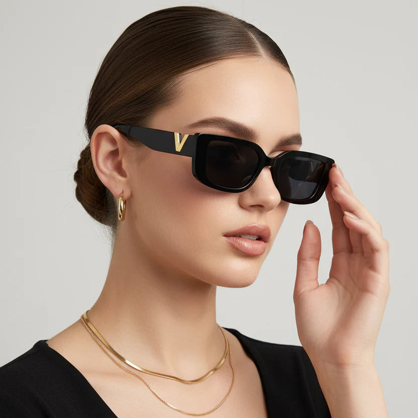 Woman wearing black sunglasses with a gold chain necklace on a neutral background